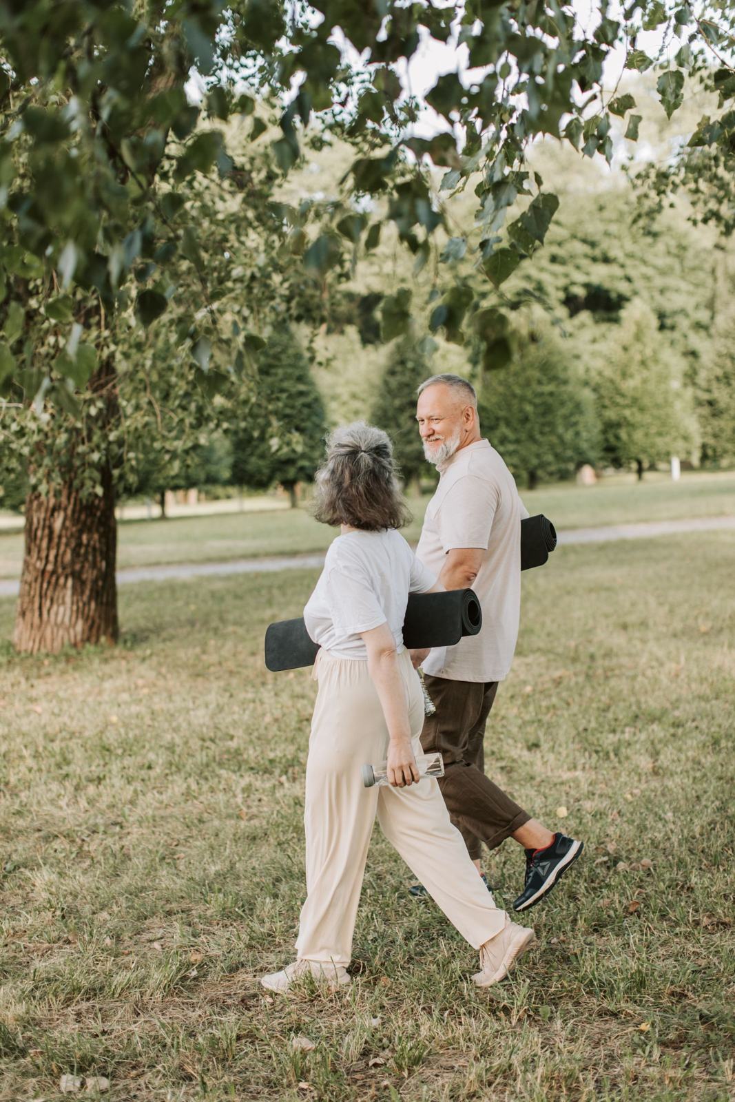 A couple walking through a park carrying exercise mats